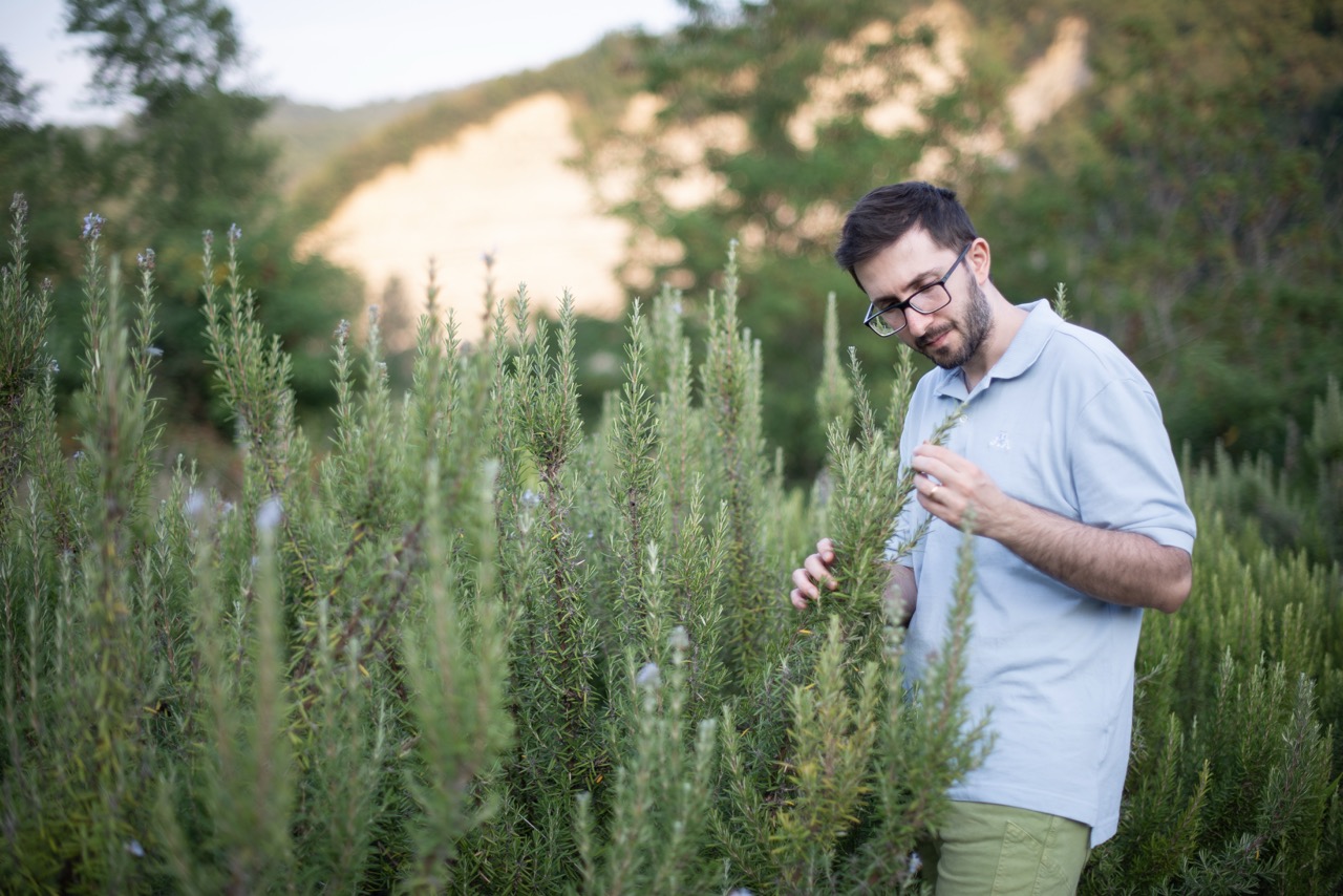 Andrea Passini osserva e annusa un rametto di rosmarino durante un momento di studio e contatto con le piante officinali.
